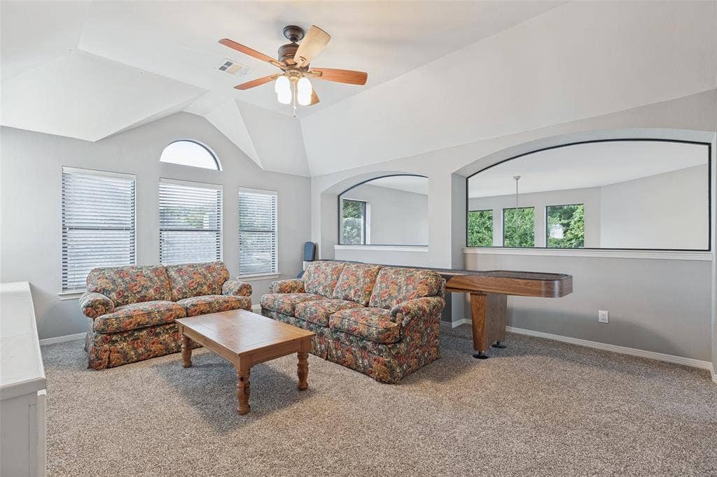 Vaulted ceiling featuring a central multi-blade ceiling fan, expansive arched windows, and decorative wall cutouts with integrated mirrors