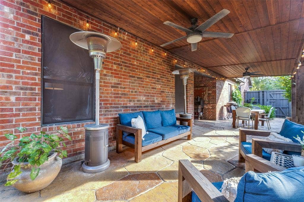 Covered patio featuring a wood-plank ceiling, exposed brick wall, natural stone patio flooring, and two ceiling fans