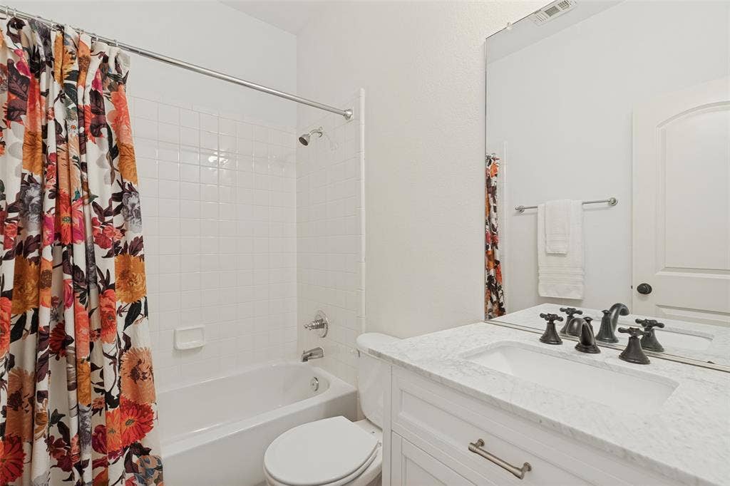 Bathroom for split bedroom featuring a white vanity with a stone-finish countertop, undermount sink, multi-handle faucet, full-height mirror, and a tub with a white tile surround