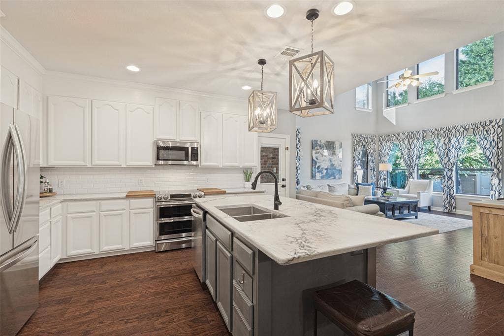 Kitchen featuring a central island with a stone countertop, white cabinetry, stainless steel appliances, geometric pendant lighting, and wood-finish flooring