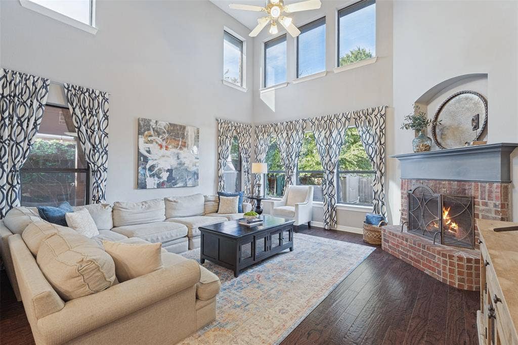 Double-height ceiling, large windows, brick fireplace with mantel, and wood-finish flooring