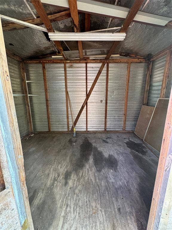 Storage structure featuring exposed wood framing, metal wall paneling, wood flooring, and overhead lighting