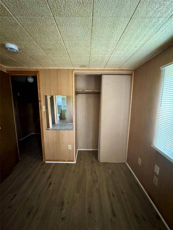 Wood-finish flooring, paneled wall surfacing, ceiling with acoustic-style panels, and built-in closet with sliding panel door