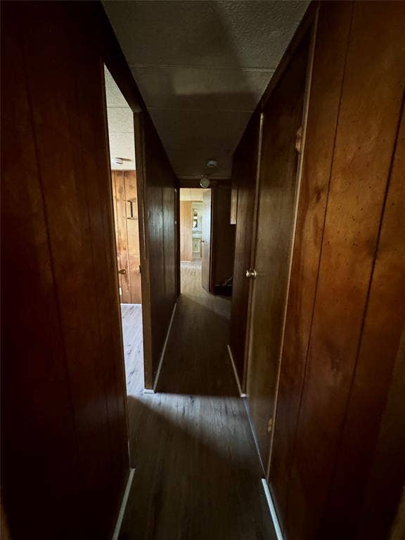 Hallway featuring wood-panel wall finishings, wood-finish flooring, and solid-core doors with metallic hardware