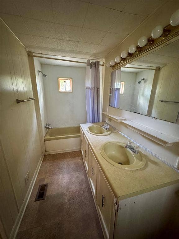 Bathroom featuring a dual-sink vanity with a wide countertop, an integrated oversized wall mirror, tile-finish flooring, and a tub-shower combination