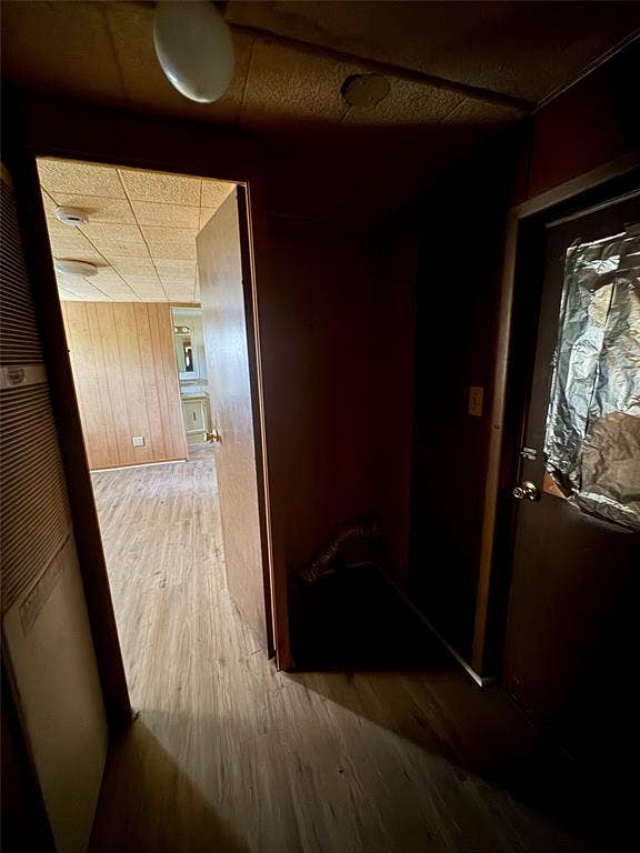 Wood-finish flooring and wood-paneled walls featuring a drop ceiling with integrated flush-mount lighting