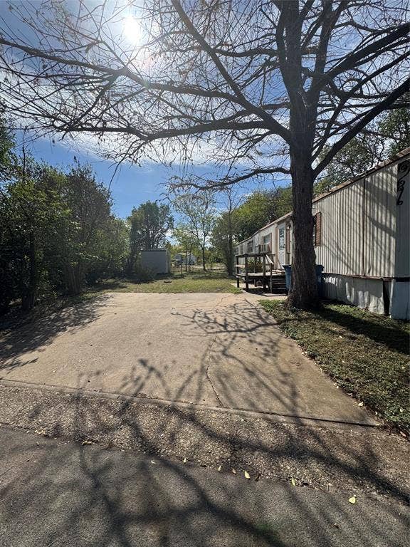 Concrete driveway, level lawn, mature trees, and detached storage structure