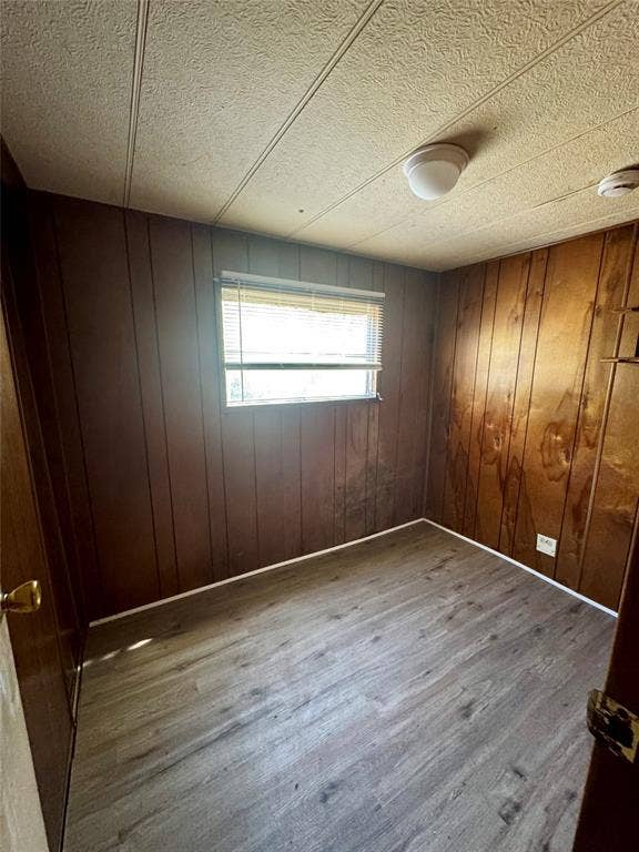 Interior room featuring wood-finish flooring, paneled walls, and a single window with horizontal blinds