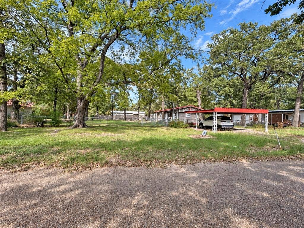 Expansive lot featuring mature trees, chain-link perimeter fencing, and a metal-roofed carport