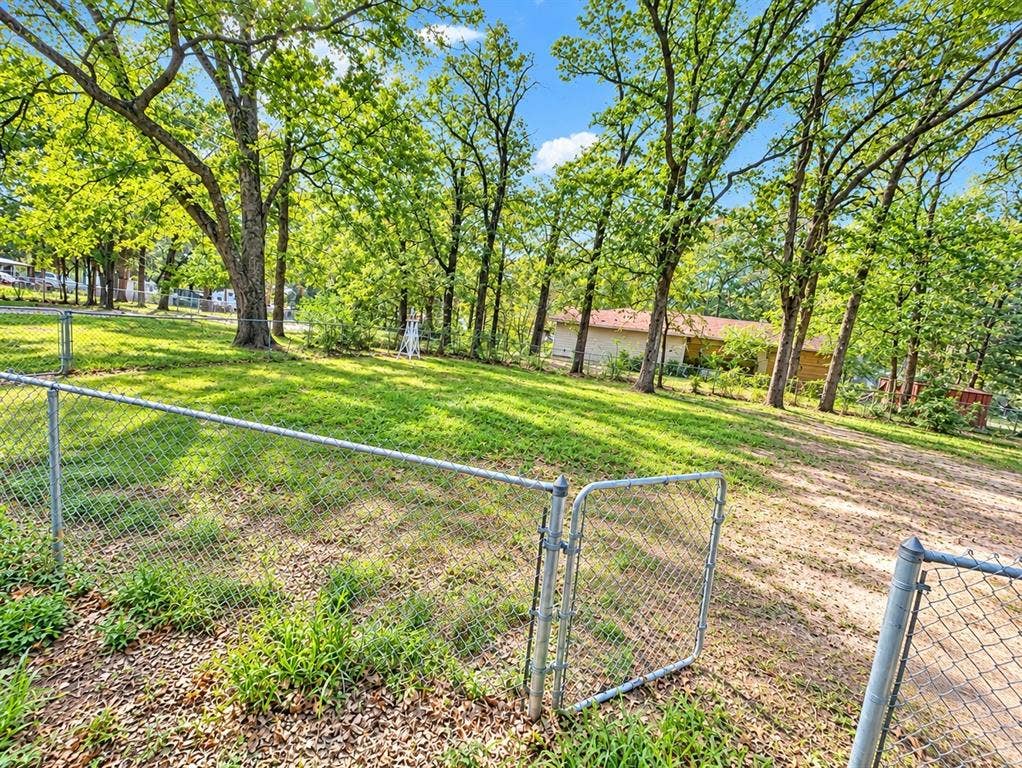 Expansive backyard featuring a fenced perimeter, mature hardwood trees, and open green space