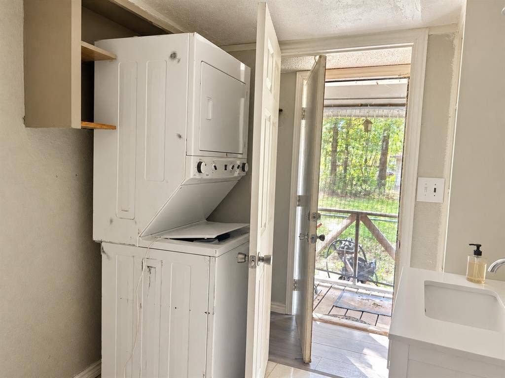 Built-in stacked laundry unit, open shelving, white vanity with integrated sink, and an exterior door with access to a deck