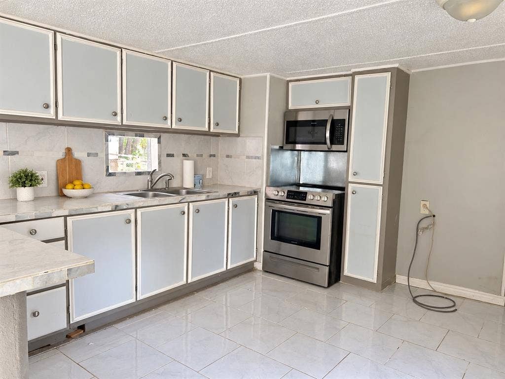 Kitchen featuring cabinetry with frosted glass inserts, stainless steel appliances, a tile backsplash, and light-toned tile flooring