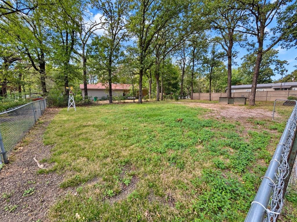 Expansive backyard featuring a chain-link perimeter fence, mature trees, and an ornamental metal windmill structure