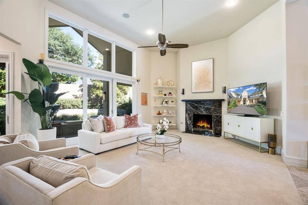 Living area featuring soaring ceilings, expansive multi-pane windows, a dark stone fireplace surround, built-in recessed shelving, and a ceiling fan