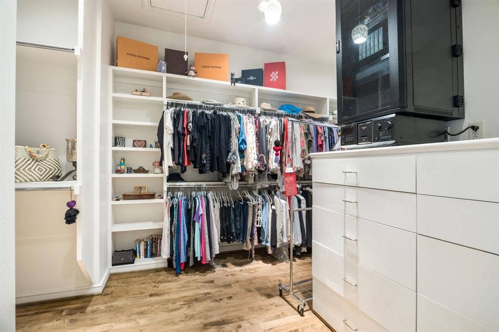Walk-in closet featuring white built-in shelving, integrated hanging rods, a multi-drawer white cabinet, and wood-finish flooring