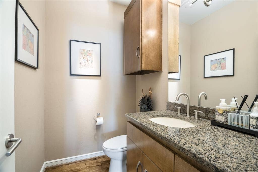 Bathroom featuring a wood-finish vanity with a stone countertop, an integrated sink with a high-arch metal faucet, a wall-mounted wooden cabinet, and wood-finish flooring