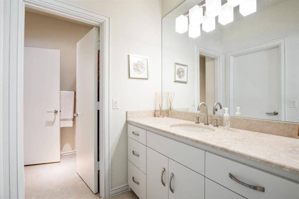 White cabinetry, neutral stone-finish countertop, undermount sink, brushed-metal hardware, and oversized wall-mounted mirror