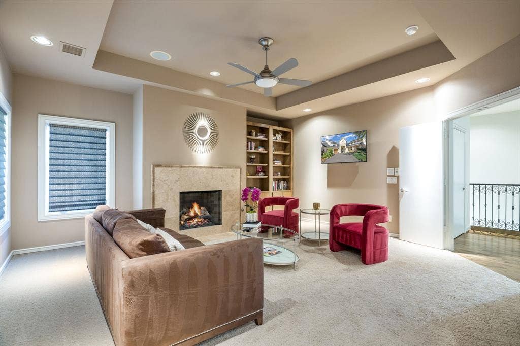 Tray ceiling with recessed lighting, stone-surround fireplace, and built-in wooden shelving