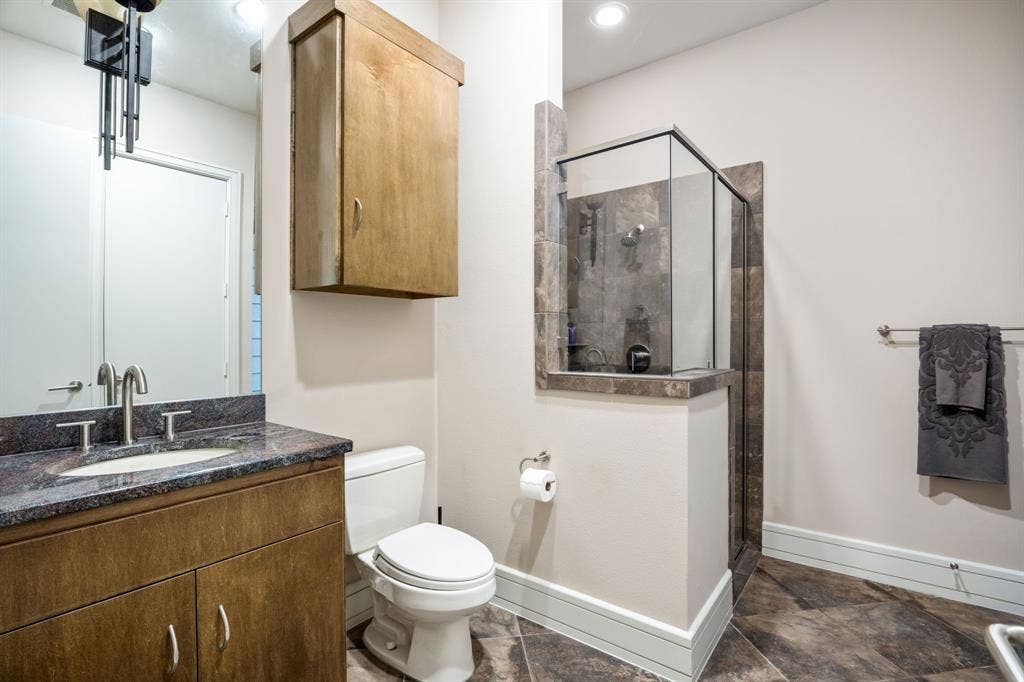 Bathroom featuring a natural wood-finish vanity, stone-topped counter with an integrated basin, wood-finish wall cabinet, and a walk-in shower with tile surround and glass enclosure