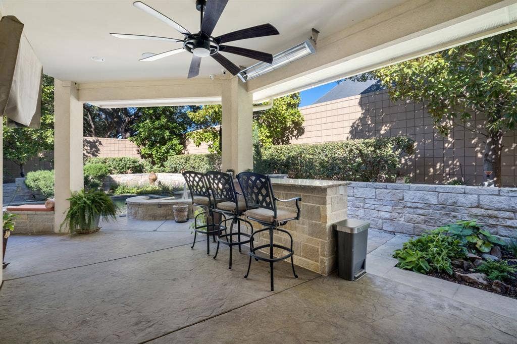 Covered patio featuring a built-in stone bar with a stone countertop, a ceiling-mounted fan, and an integrated overhead radiant heater