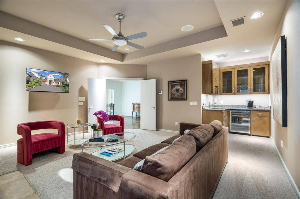 Tray ceiling with integrated recessed lighting, ceiling fan, carpeted flooring, and built-in wet bar featuring cabinetry with glass-front uppers and stone countertops