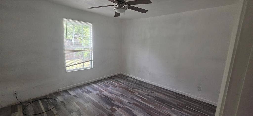3510 Marshall Street, Greenville, TX 75401 Room featuring wood-finish flooring, neutral wall paint, and a ceiling fan with integrated lighting, completed by a multi-pane window