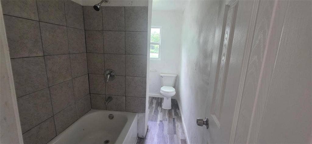 3510 Marshall Street, Greenville, TX 75401 Bathroom featuring a porcelain tub with a chrome shower fixture, tiled surround, wood-finish flooring, and a standard toilet
