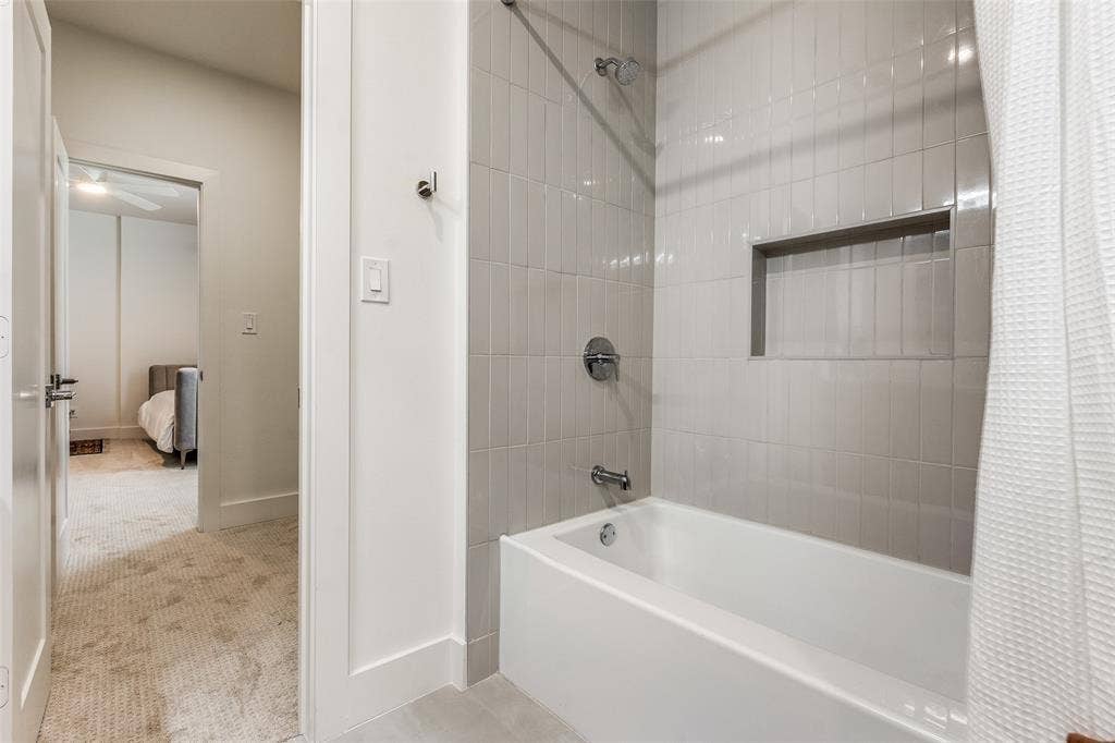 Bathroom featuring a white bathtub, vertical tile shower surround, integrated wall niche, and polished chrome plumbing fixtures