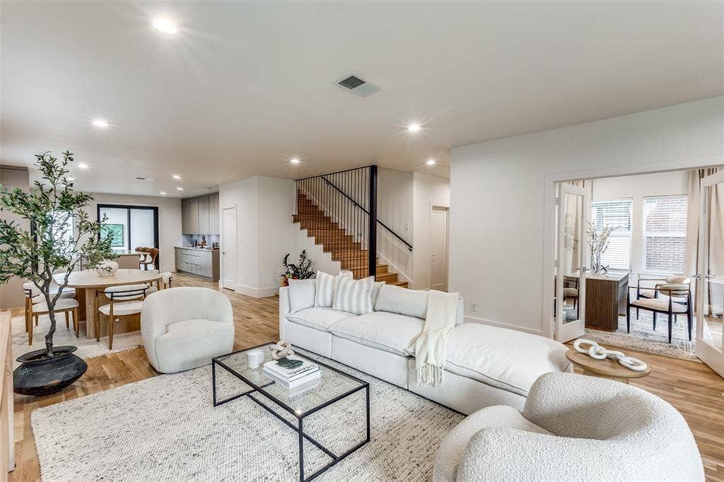 Open-concept floor plan featuring wood-finish flooring, recessed lighting, a staircase with metal railings, and double glass-paned doors