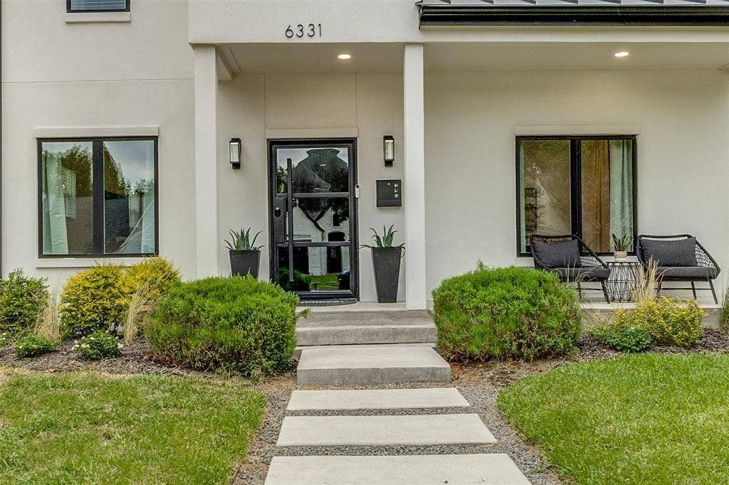 Contemporary exterior featuring smooth stucco facade, concrete paver walkway, modern glass-paned entry door, and recessed porch lighting