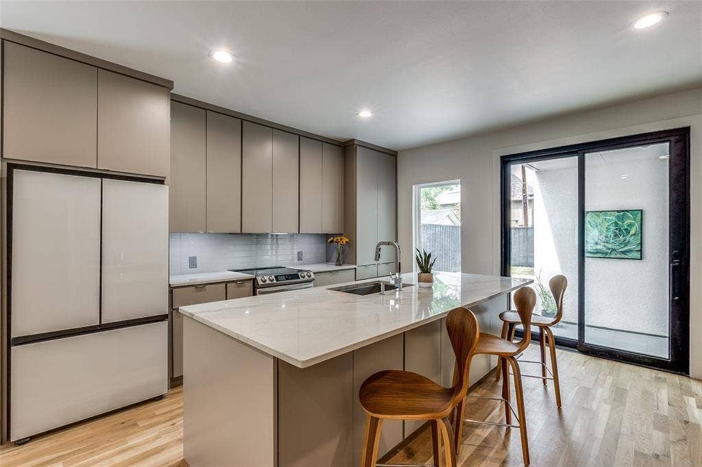 Kitchen featuring flat-panel cabinetry, a central island with a stone-finish countertop, stainless steel undermount sink, integrated refrigerator, and wood-finish flooring
