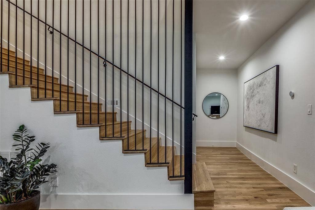 Staircase featuring wood-finish treads, vertical black metal balusters, integrated recessed lighting, and wood-finish flooring