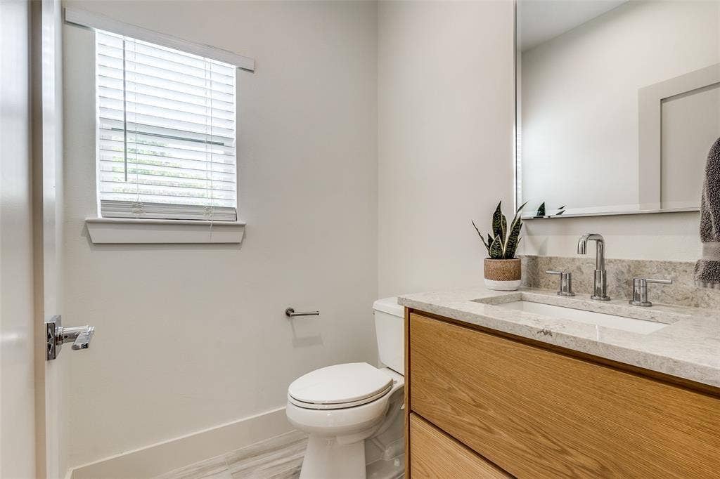 Wood-finish vanity cabinet, stone-finish countertop, undermount sink with polished chrome hardware, and large wall-mounted mirror