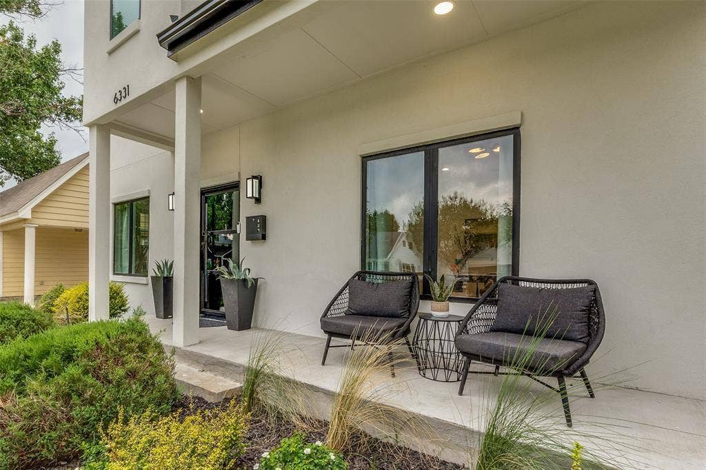 Covered concrete porch with smooth stucco exterior, dark-framed windows, and minimalist wall-mounted light fixtures