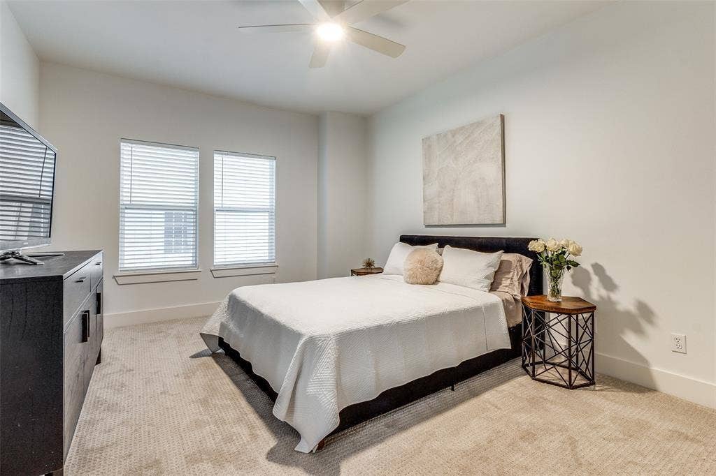 Neutral-toned room featuring plush carpeting, dual windows with horizontal blinds, and a ceiling-mounted fan with integrated lighting