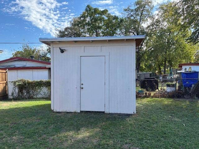 Detached storage structure featuring vertical siding, a flat roof, a solid entry door, and an exterior light fixture