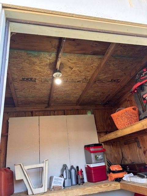 Storage structure featuring exposed wood framing, built-in wooden shelving, and a ceiling-mounted light fixture