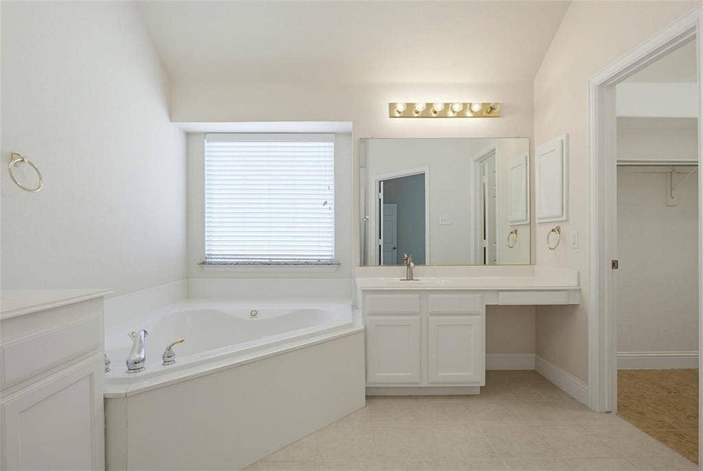 4402 Horizon Drive, Garland, TX 75043 Corner soaking tub featuring a deck-mounted chrome faucet, white cabinetry with a built-in vanity, large vanity mirror, and wall-mounted light fixture