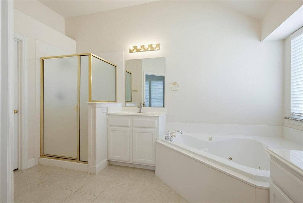 4402 Horizon Drive, Garland, TX 75043 Bathroom featuring a jetted soaking tub, a separate walk-in shower with a gold-tone frame, a white vanity cabinet, a wall-mounted light fixture, and tile flooring
