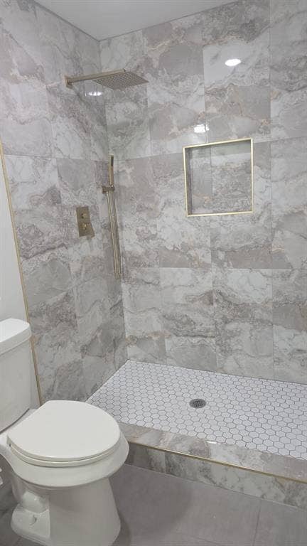 4643 Luzon Street, Dallas, TX 75216 Walk-in shower featuring large-format patterned wall tile, white hexagonal floor tile, recessed wall niche, rainfall showerhead, and gold-finish fixtures