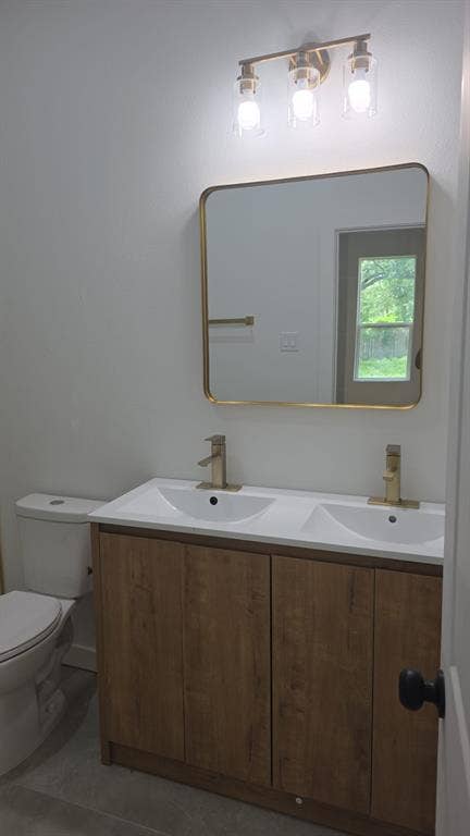 4643 Luzon Street, Dallas, TX 75216 Double-sink vanity with wood-finish cabinetry, metal-finish hardware, rectangular mirror with rounded corners, and three-light glass fixture