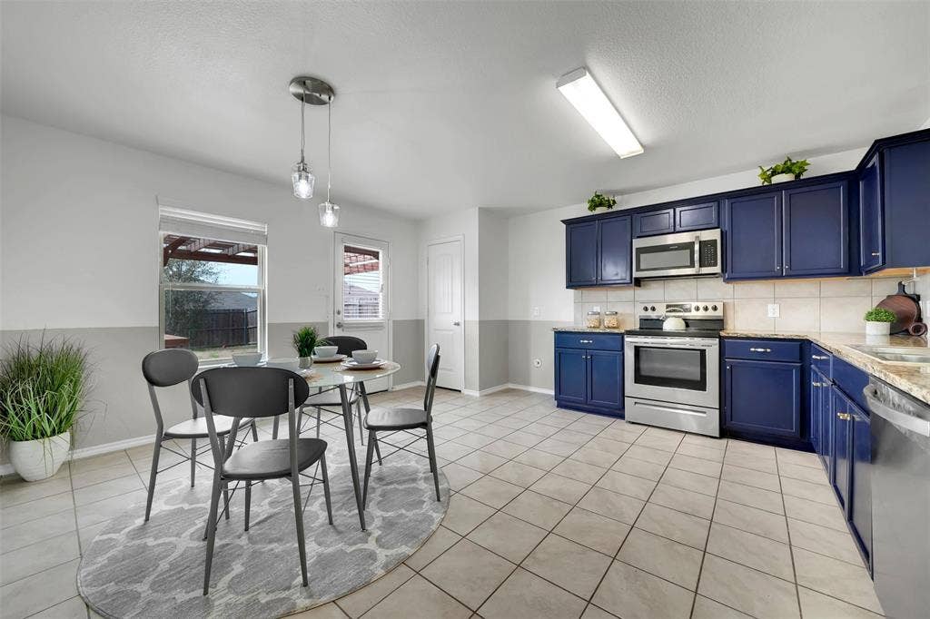 1121 Basswood Lane, Royse City, TX 75189 Kitchen featuring blue cabinets, backsplash, stainless steel appliances, light countertops, and light tile patterned floors