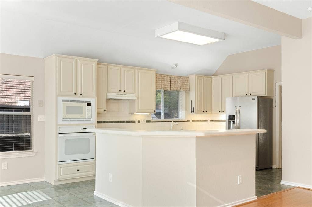 2803 Pheasant Run Drive, McKinney, TX 75072 Kitchen featuring cream-colored cabinetry, a peninsula countertop, built-in wall oven and microwave, stainless steel refrigerator, and tiled flooring