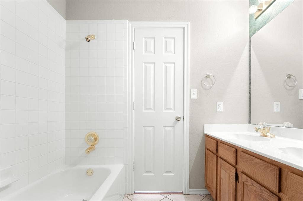 2803 Pheasant Run Drive, McKinney, TX 75072 Bathroom featuring a dual-basin vanity with wood-finish cabinetry, white solid-surface countertop, gold-toned hardware, and a tile-surround shower and tub combination