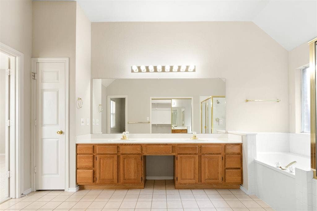 2803 Pheasant Run Drive, McKinney, TX 75072 Dual-vanity cabinetry with a central seated vanity area, expansive wall-to-wall mirror, multi-bulb overhead lighting, and built-in soaking tub