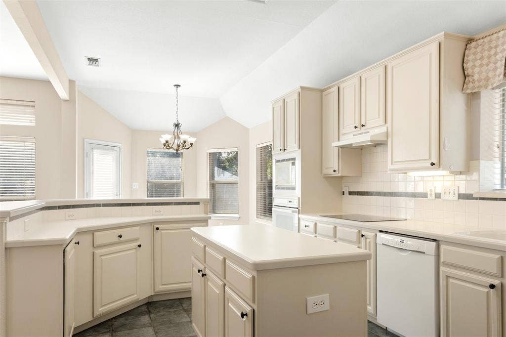 2803 Pheasant Run Drive, McKinney, TX 75072 Kitchen featuring off-white cabinetry, central island, integrated wall oven, tile backsplash with decorative inlay, and vaulted ceiling