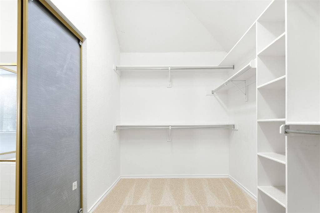 2803 Pheasant Run Drive, McKinney, TX 75072 Walk-in closet featuring vaulted ceilings, floor-to-ceiling built-in shelving, dual-level metal hanging rods, and neutral carpeting