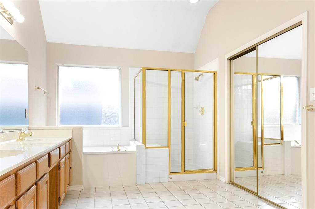 2803 Pheasant Run Drive, McKinney, TX 75072 Bathroom featuring a vaulted ceiling, soaking tub, glass-enclosed shower with metal framing, vanity with wooden cabinetry, and sliding mirrored wardrobe doors