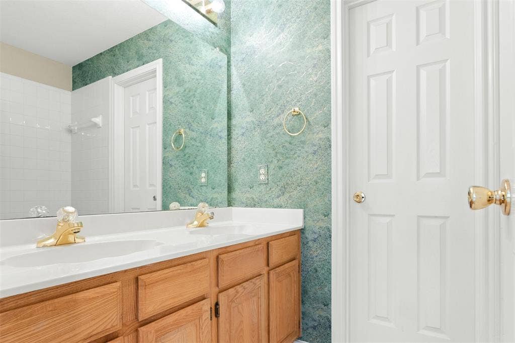 2803 Pheasant Run Drive, McKinney, TX 75072 Dual-sink vanity with white countertop, large frameless mirror, and metallic gold-finish fixtures