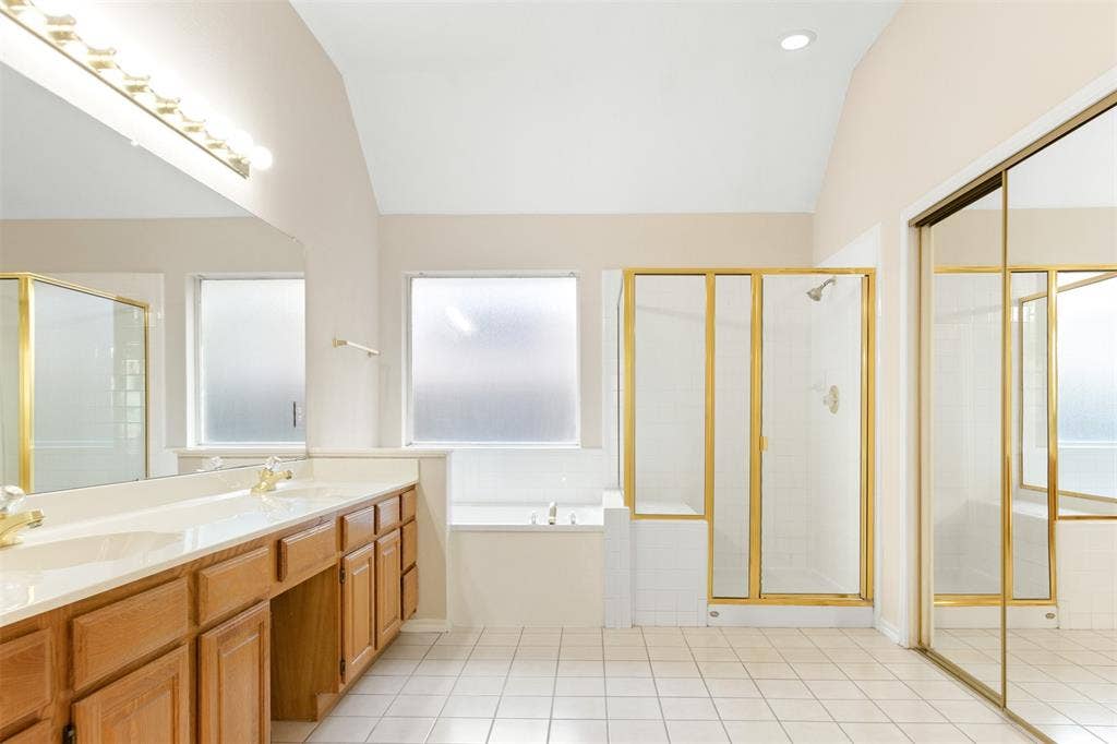 2803 Pheasant Run Drive, McKinney, TX 75072 Bathroom featuring a dual-sink vanity, tiled floor, glass-enclosed shower, soaking tub, and vaulted ceiling